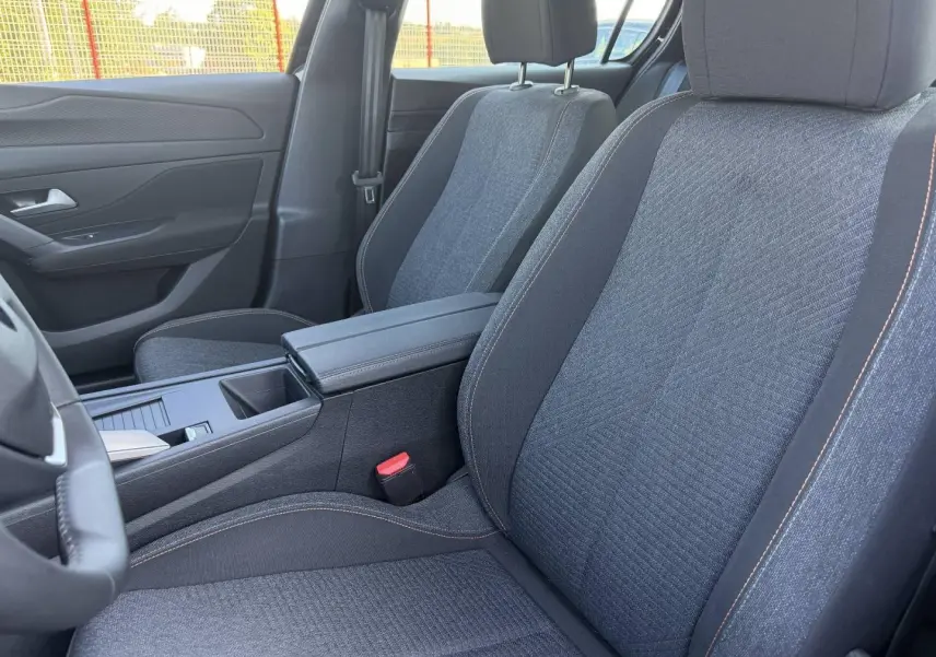 Vue intérieure rapprochée des sièges avant en tissu gris avec surpiqûres orange de la Peugeot e-308 2025.