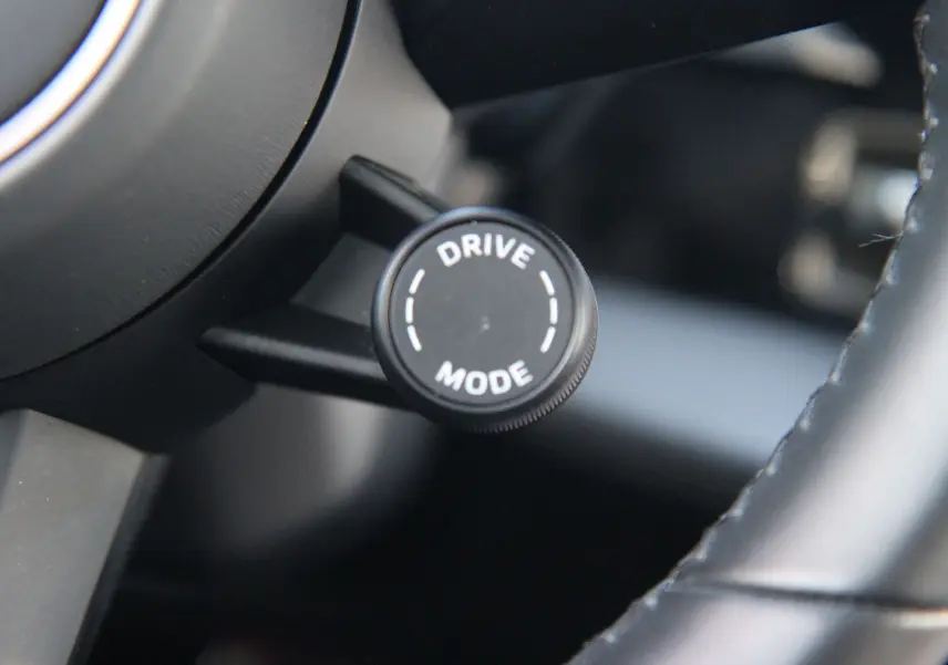 Gros plan sur le bouton rotatif "Drive Mode" noir situé derrière le volant en cuir noir du Porsche Taycan Turbo 2020.