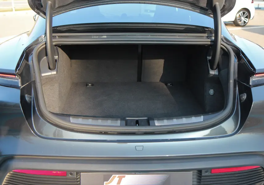 Coffre ouvert vu de l'arrière d'une Porsche Taycan Turbo gris anthracite, montrant l'espace de rangement vide.