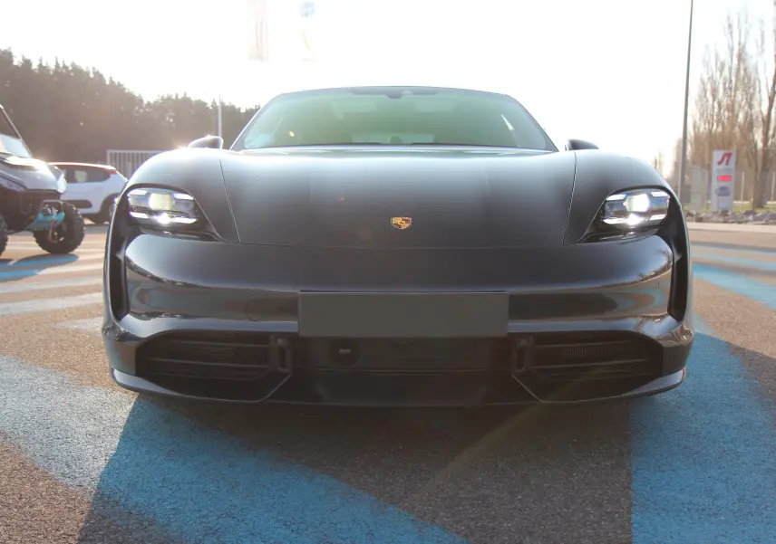 Vue frontale d'une Porsche Taycan Turbo gris anthracite avec phares LED allumés et logo Porsche visible sur le capot.