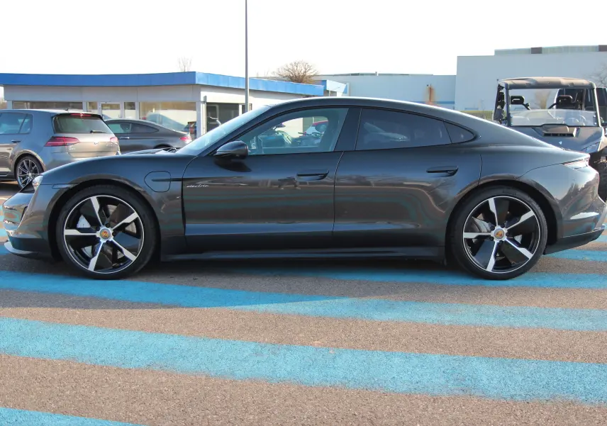 Profil côté gauche d'une Porsche Taycan Turbo gris anthracite avec jantes exclusives 21 pouces sur parking extérieur.