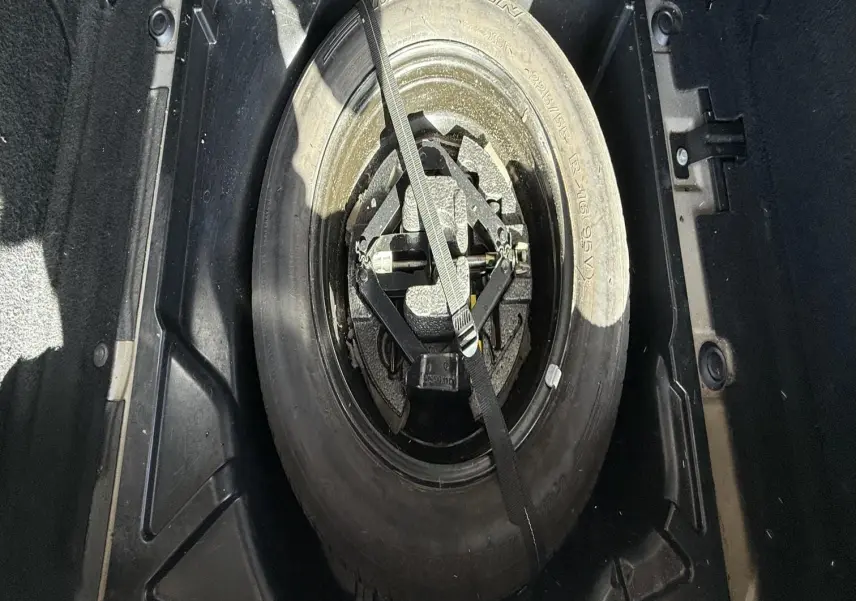 Vue plongeante sur la roue de secours Michelin et son équipement de levage dans le coffre d'une Peugeot 607 grise.