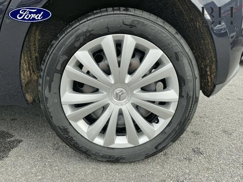 Gros plan sur la roue avant gauche d'une Citroën C3 bleu encre avec enjoliveur argenté à rayons fins.