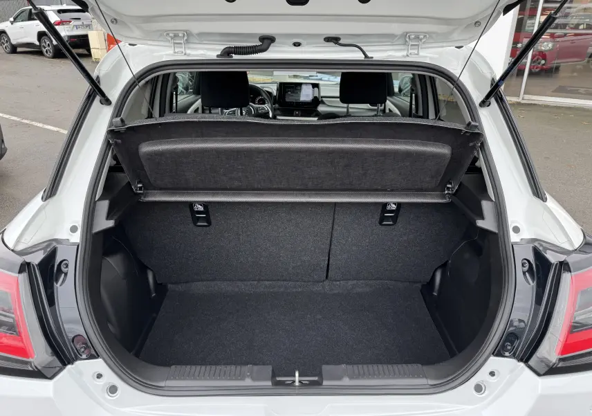 Coffre ouvert vu de l'arrière d'une Suzuki Swift 1.2 Privilège Hybrid blanche, avec cache-bagages relevé.