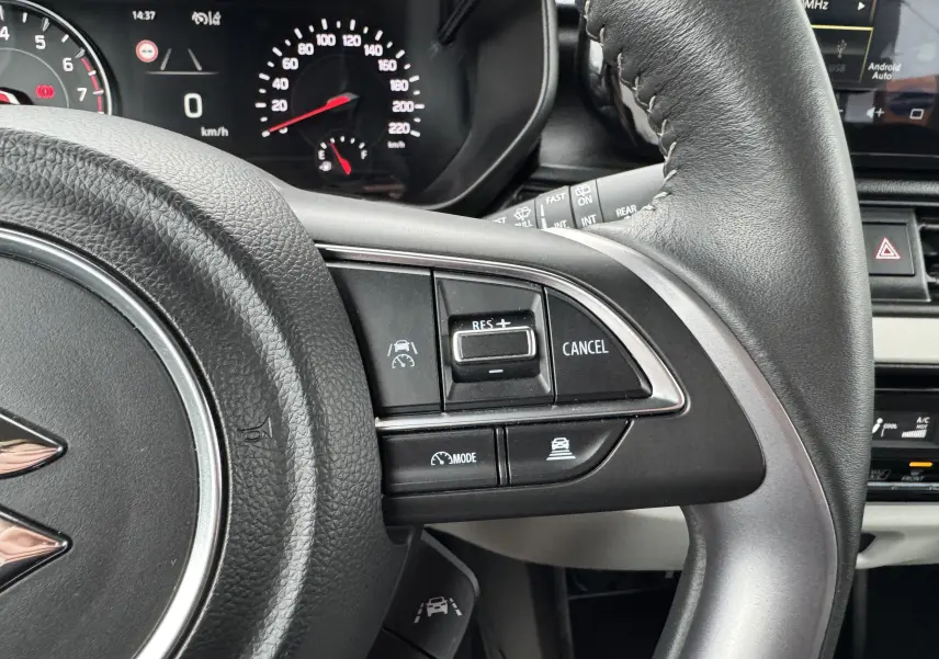 Gros plan sur les commandes de régulateur de vitesse au volant cuir noir de la Suzuki Swift 1.2 Privilège Hybrid blanche.