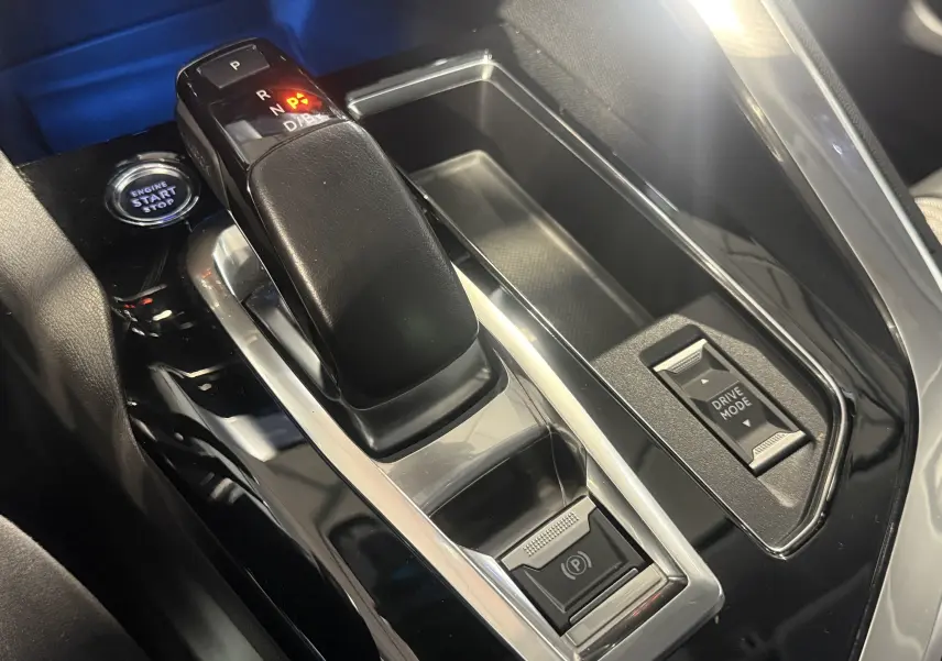 Gros plan sur la console centrale noire du Peugeot 3008 Hybrid 2025 avec levier de vitesse automatique et bouton Drive Mode.