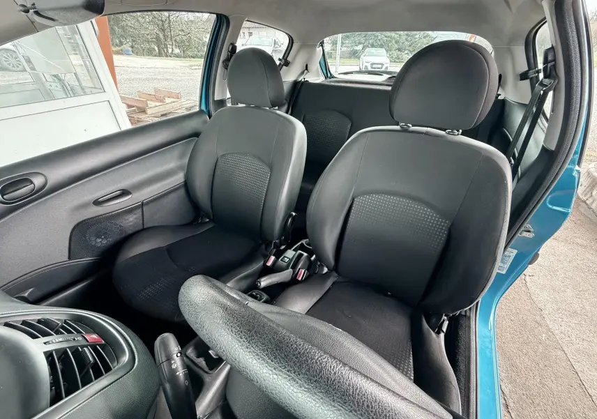 Vue intérieure avant de la Peugeot 206+ bleue, montrant le tableau de bord et le volant côté gauche avec porte ouverte.
