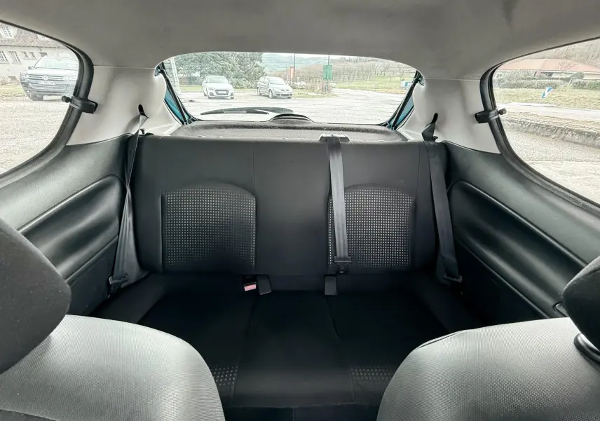 Vue intérieure avant droite de la Peugeot 206+ bleue de 2011, montrant les sièges noirs en tissu et cuir et le volant.