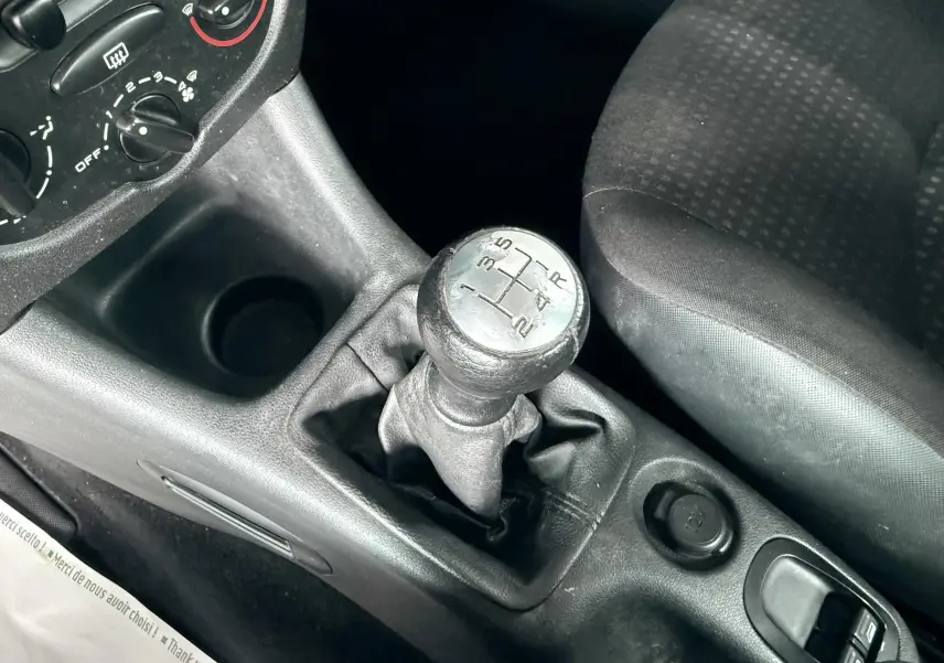 Détail de la console de climatisation noire de la Peugeot 206+ 1.1 essence, avec commandes rotatives et écran multimédia partiel.