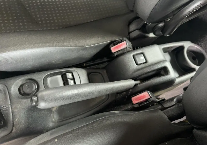 Gros plan sur la console centrale noire de la Peugeot 206+ 2011, montrant les commandes de vitres électriques et prise 12V.