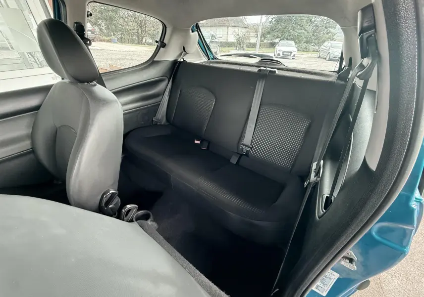 Vue intérieure côté conducteur d'une Peugeot 206+ bleue de 2011 avec sièges tissu noir et volant cuir.