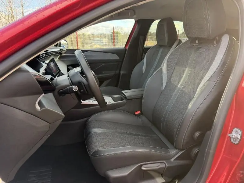 Vue intérieure côté conducteur de la Peugeot 308 2024 rouge Elixir, montrant les sièges et le tableau de bord moderne.