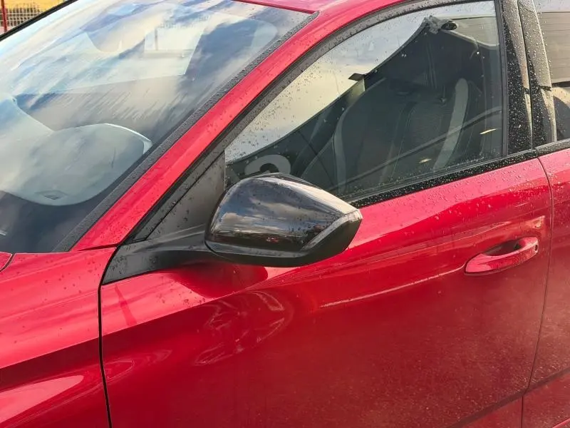 Détail du côté gauche avant d’une Peugeot 308 2024 Rouge Elixir avec rétroviseur noir et pluie visible sur la carrosserie.