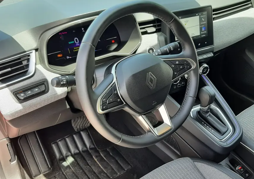Vue intérieure du poste de conduite de la Renault Clio V rouge flamme, avec volant multifonction et écran tactile central.