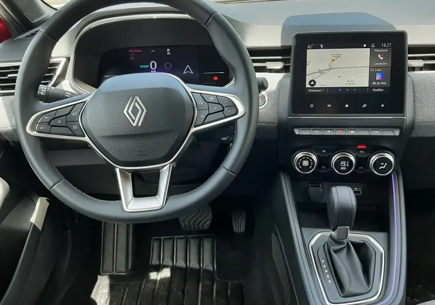 Vue intérieure avant de la Renault Clio V E-Tech, volant multifonction, écran tactile central et levier de boîte auto.