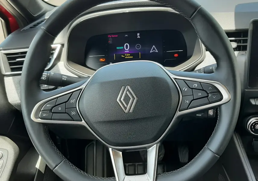 Vue rapprochée du volant noir de la Renault Clio V hybride 2025 avec tableau de bord digital allumé.