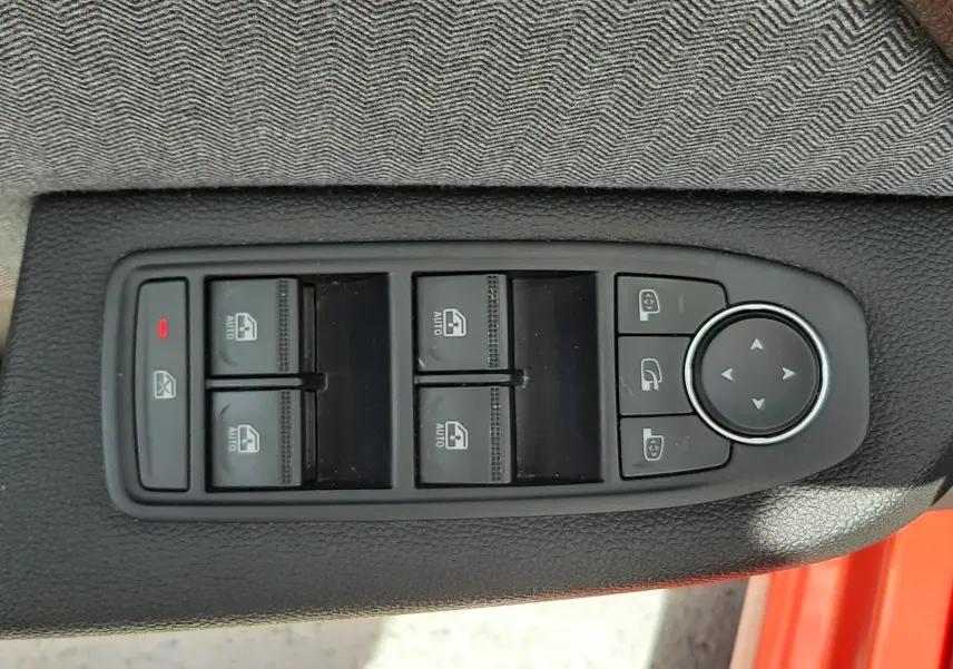Vue rapprochée des commandes de lève-vitres et rétroviseurs sur la porte côté conducteur d’une Renault Clio V rouge flamme.
