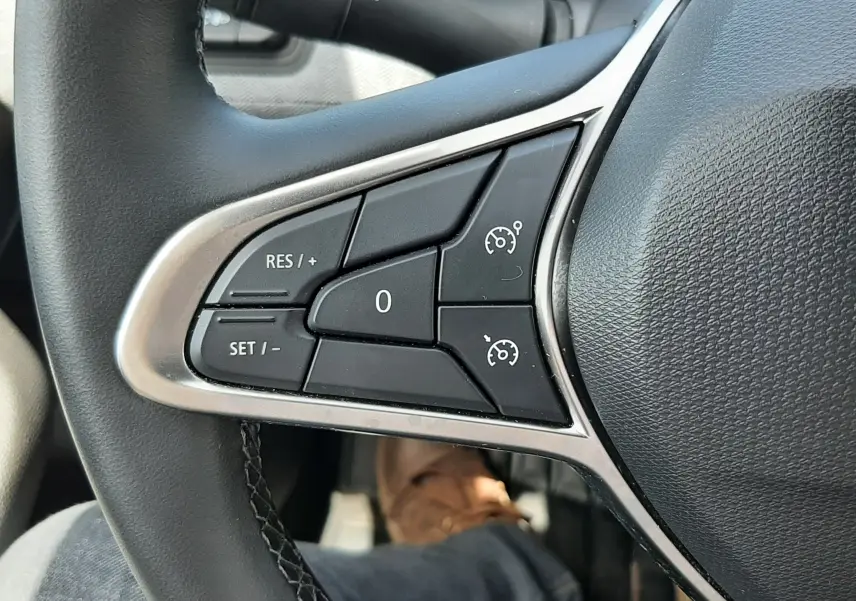 Gros plan sur les commandes au volant côté gauche de la Renault Clio V, finition gris noir, boutons de régulateur de vitesse.