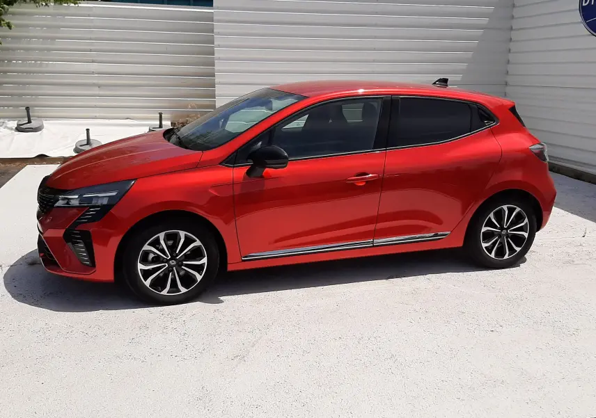 Profil droit d'une Renault Clio V rouge flamme métal, avec jantes alliage noires et détails chromés sous les portes.