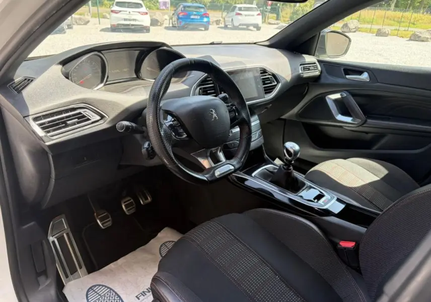 Vue intérieure côté conducteur de la Peugeot 308 GT-Line 2017, avec volant cuir, levier de vitesses manuel et sièges noirs.