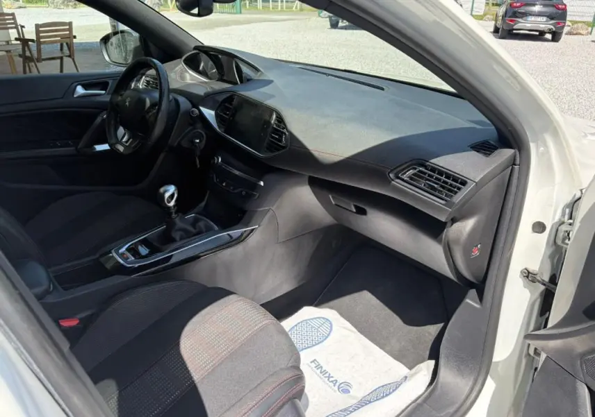 Intérieur de la Peugeot 308 GT-Line 2017 vue côté passager, avec tableau de bord noir et sièges tissu noir à surpiqûres rouges.