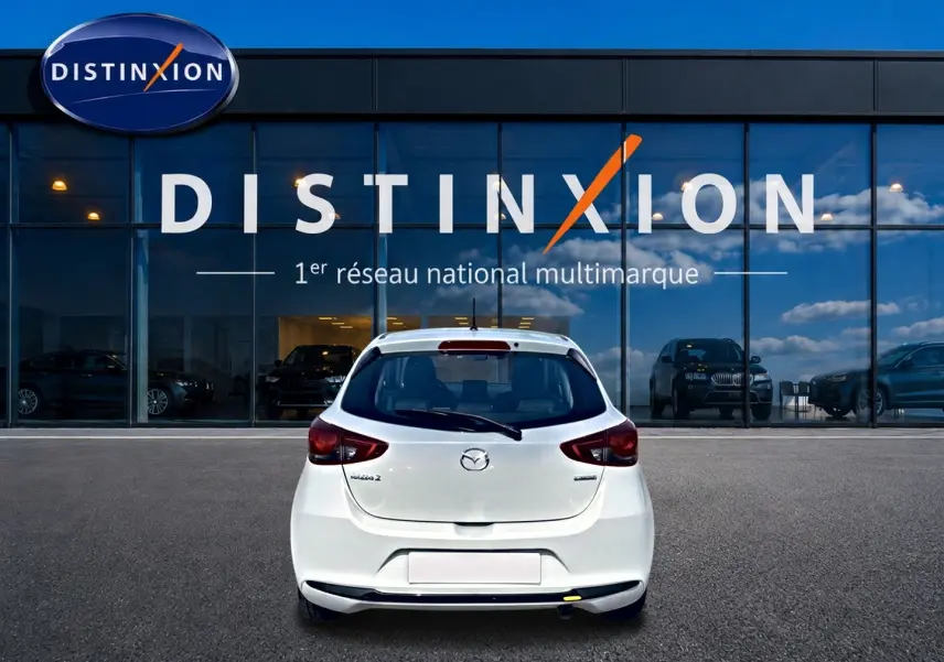 Vue arrière d'une Mazda2 blanche 2024 stationnée devant une vitrine avec logo Distinxion.