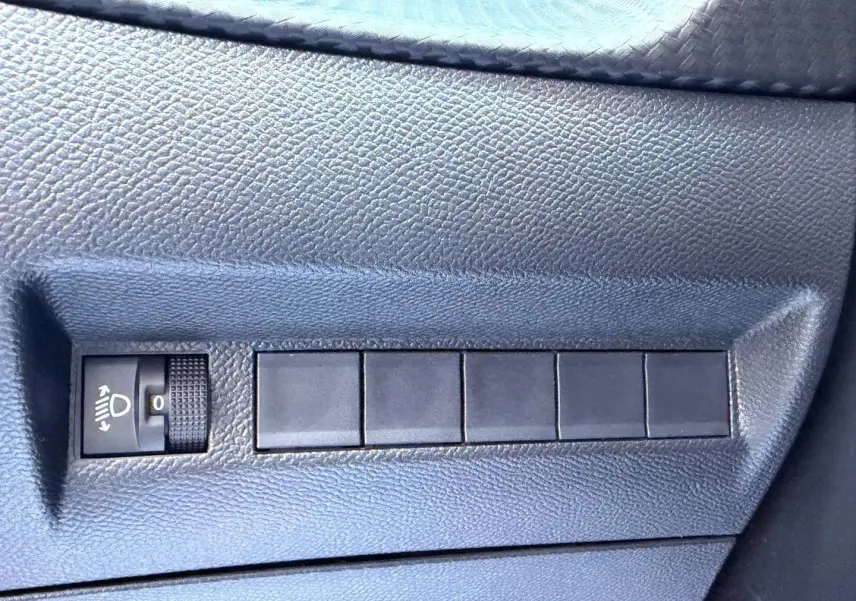 Gros plan sur le panneau de réglage des phares et boutons noirs sur la portière côté conducteur du Peugeot 208 gris Artense.