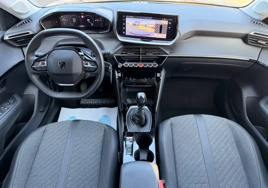 Vue intérieure frontale du poste de conduite du Peugeot 208 1.2 100ch gris Artense avec volant compact et écran tactile central.