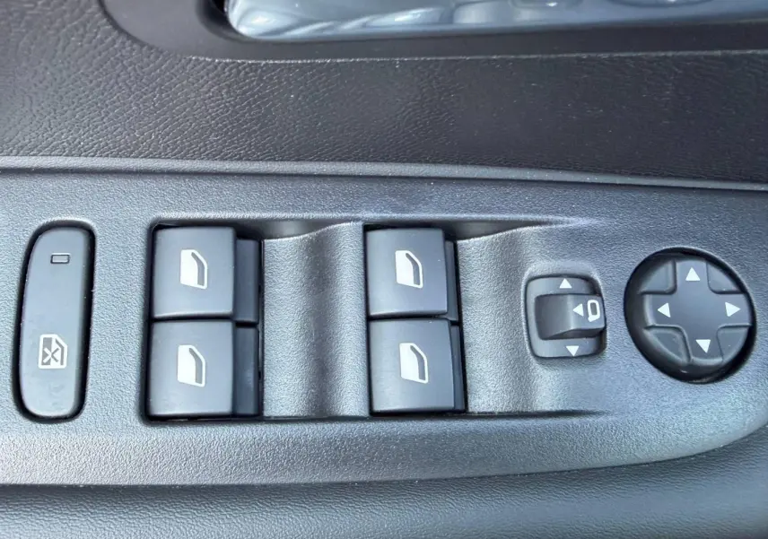 Gros plan sur les commandes de lève-vitres et réglage des rétroviseurs côté conducteur dans l’habitacle noir du Peugeot 208 gris Artense.
