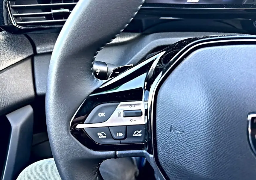 Gros plan sur le volant multifonction noir de la Peugeot 308 1.5 BlueHDi 130 Allure, avec commandes intégrées.