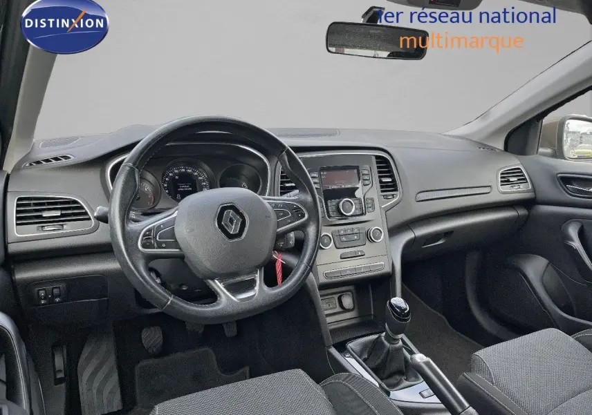 Vue intérieure avant de la Renault Mégane IV TCe 100 Life, tableau de bord et volant noirs avec levier de vitesse manuel.