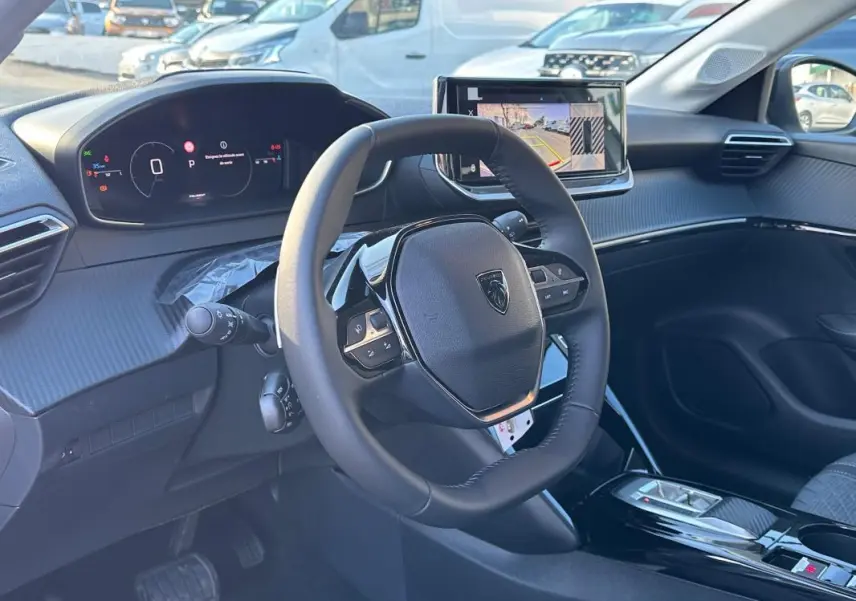 Vue intérieure du poste de conduite de la Peugeot 208 Hybrid 110 e-DCS6 Allure 2025, avec volant multifonction et écran tactile.