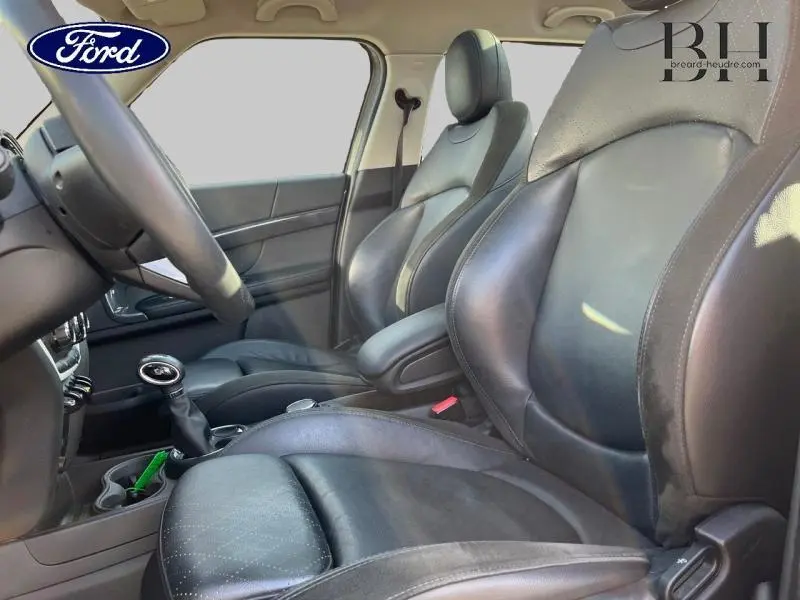 Vue intérieure côté conducteur des sièges en cuir noir du MINI Countryman Cooper SE avec accoudoir central et volant visible.