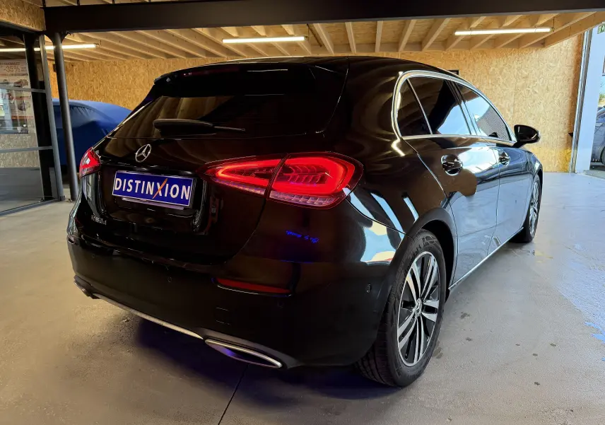 Vue 3/4 arrière droite d'une Mercedes Classe A noire avec jantes alu et sorties d'échappement chromées en intérieur garage.