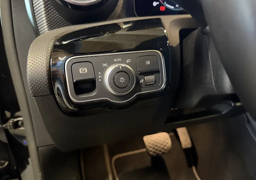 Gros plan sur les commandes d’éclairage et frein de stationnement à gauche du volant dans une Mercedes Classe A noire 2022.