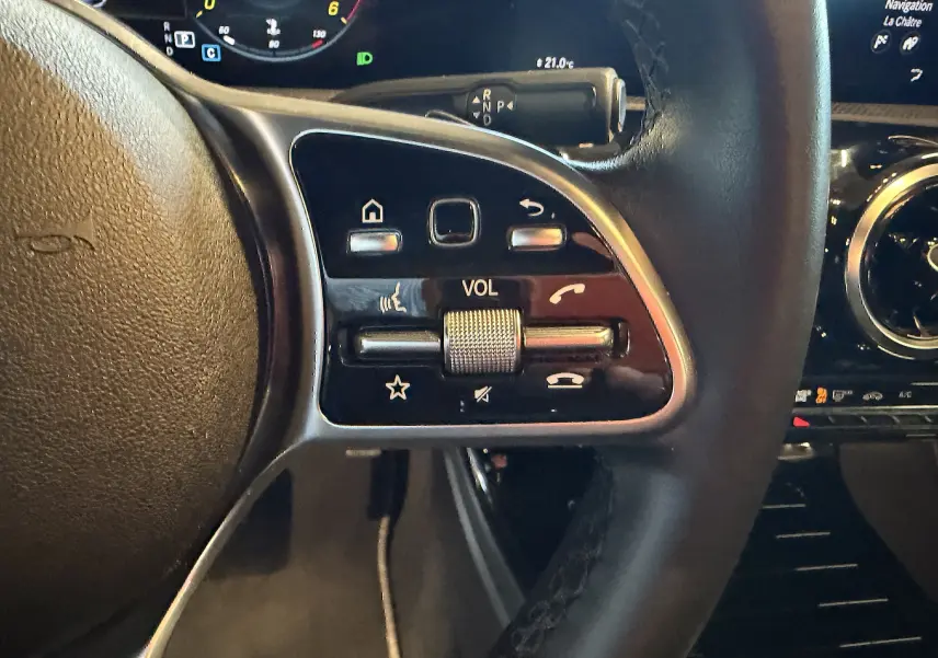Gros plan sur les commandes multifonctions du volant cuir noir d'une Mercedes Classe A 2022, avec affichage numérique en arrière-plan.
