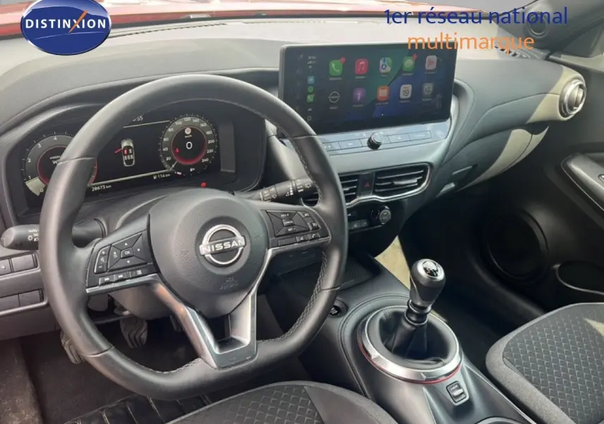 Vue intérieure du poste de conduite du Nissan Juke rouge Fuji Metal 2024, avec volant cuir et levier de vitesse manuel.
