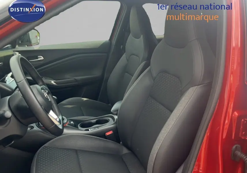 Vue intérieure côté conducteur du Nissan Juke rouge Fuji Metal 2024, montrant les sièges noirs et le volant multifonction.