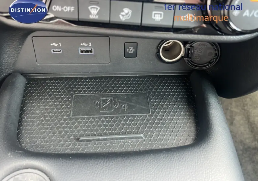 Gros plan sur la console centrale du Nissan Juke rouge Fuji Metal 2024, montrant ports USB, prise 12V et zone de recharge sans fil.