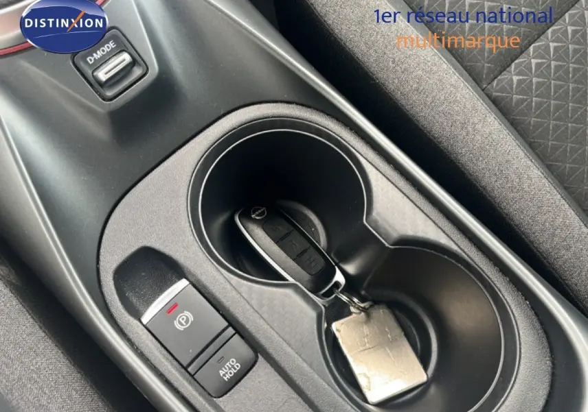 Gros plan sur la console centrale du Nissan Juke rouge Fuji Metal 2024 avec clé dans porte-gobelets et bouton frein à main.