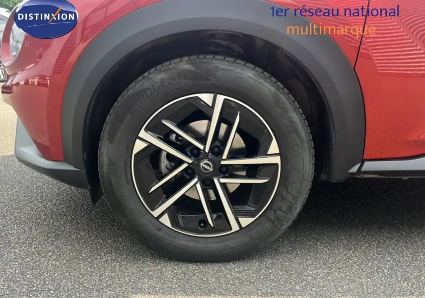 Gros plan sur la roue avant gauche du Nissan Juke rouge Fuji Metal 2024 avec jante alliage noire et argent.