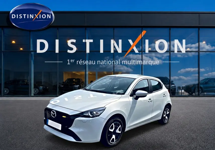 Vue 3/4 avant droite d'une Mazda2 blanche 2024 avec calandre noire et jantes au design moderne devant un showroom Distinxion.