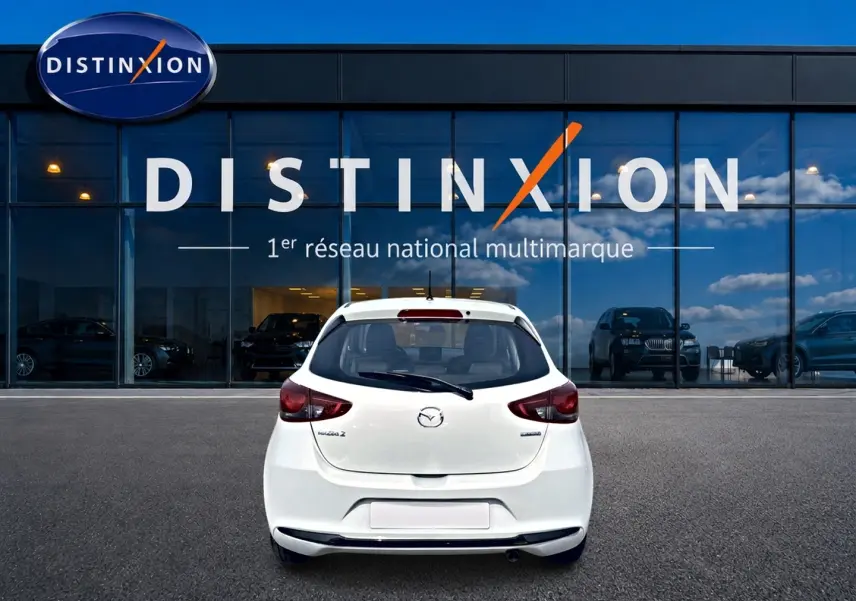 Vue arrière d'une Mazda2 blanche 2024 garée devant une vitrine avec logo Distinxion en arrière-plan.