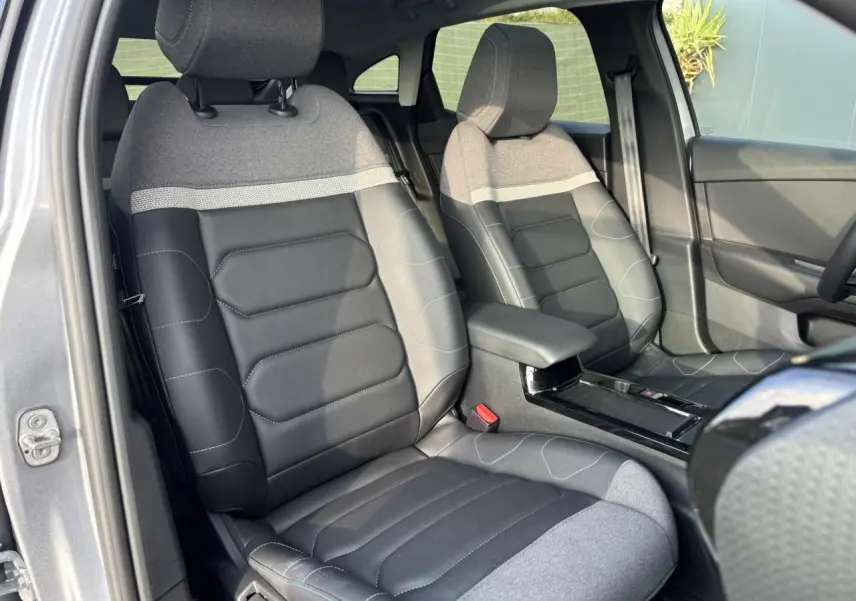 Vue intérieure avant des sièges gris et noirs de la Citroën C4 2024 avec accoudoir central et garniture tissu et cuir.