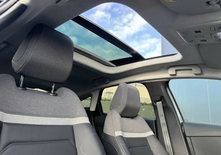 Vue intérieure avant des sièges gris chiné avec toit ouvrant panoramique ouvert sur ciel bleu.