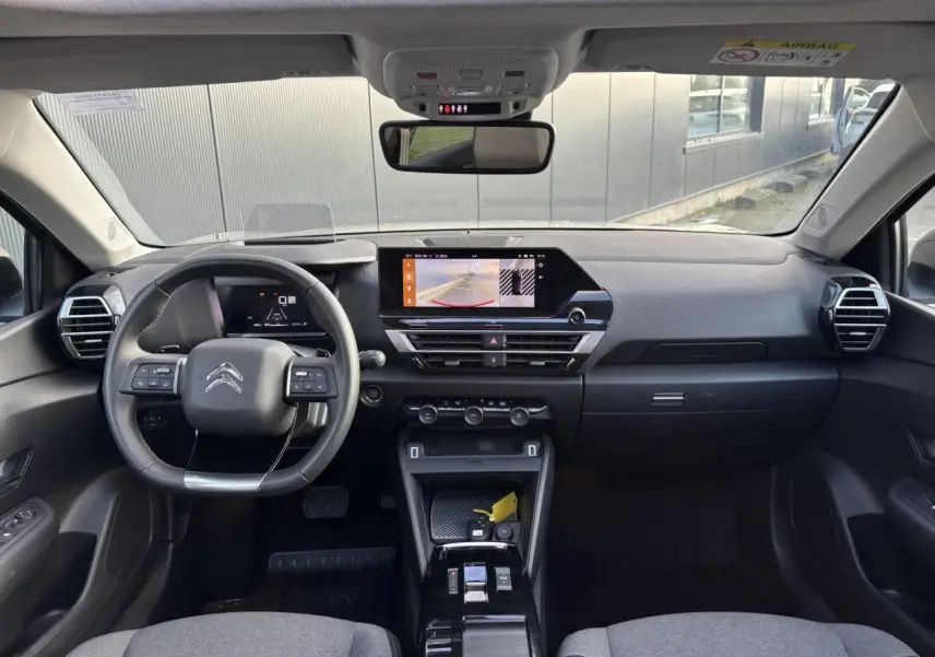 Vue intérieure avant de la Citroën C4 2024 avec tableau de bord gris, écran tactile affichant la caméra de recul et volant cuir noir.