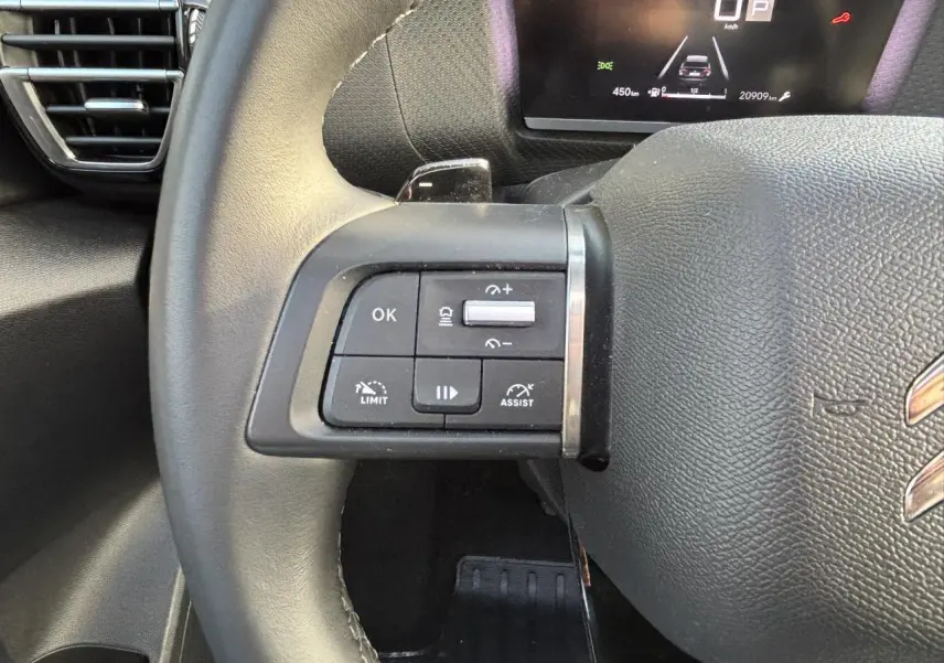 Gros plan sur les commandes au volant gauche en cuir noir du Citroën C4 2024 avec affichage numérique en arrière-plan.