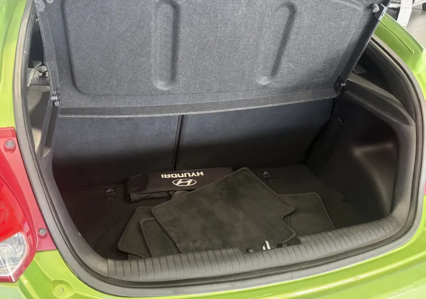 Coffre ouvert vu de l'arrière d'une Hyundai Veloster 2025 vert, avec tapis de sol et trousse Hyundai visibles à l'intérieur.
