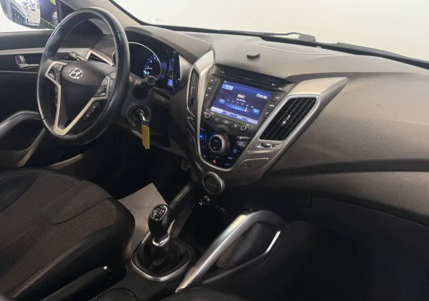 Vue intérieure côté conducteur du Hyundai Veloster 2025, avec tableau de bord noir et levier de vitesses manuel visible.