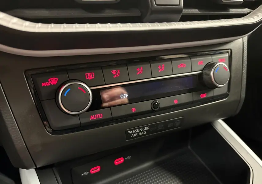 Gros plan sur la console centrale du SEAT Arona 2025, montrant les commandes de climatisation avec éclairage rouge.